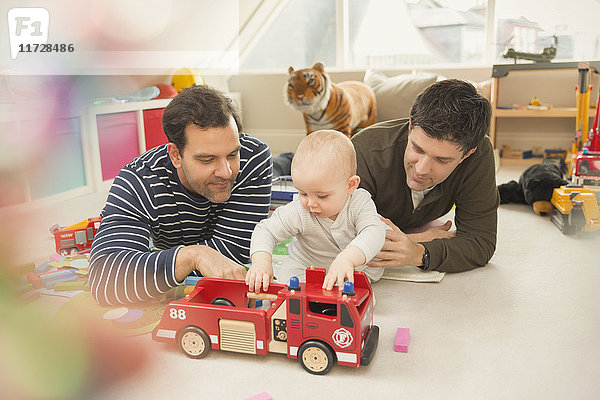 Männliche schwule Eltern und Baby-Sohn spielen mit Feuerwehrspielzeug im Spielzimmer
