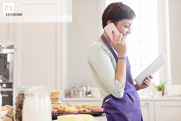 Weibliche Caterer backen  telefonieren und digitales Tablett in der Küche benutzen