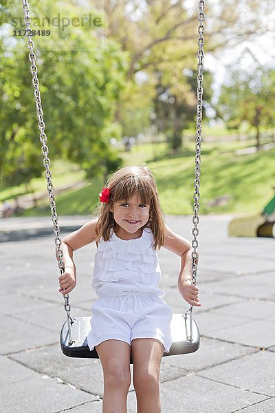 Süßes Mädchen im Park auf Schaukel lächelnd vor der Kamera