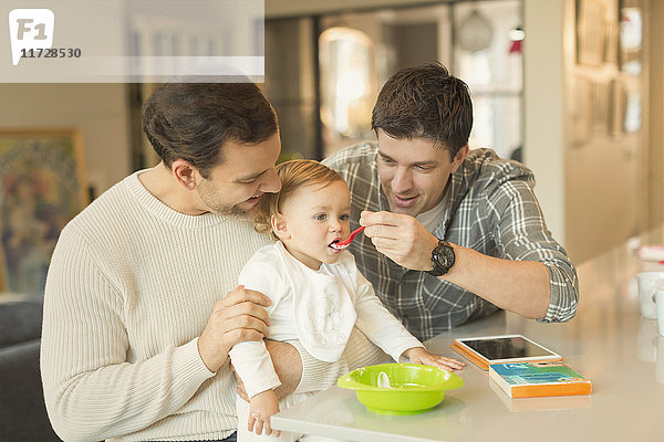Männliche schwule Eltern füttern Baby-Sohn in der Küche