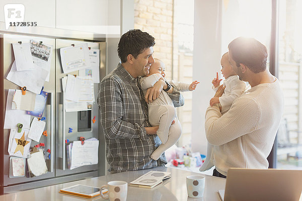 Männliche schwule Eltern halten Babysöhne in der Küche.