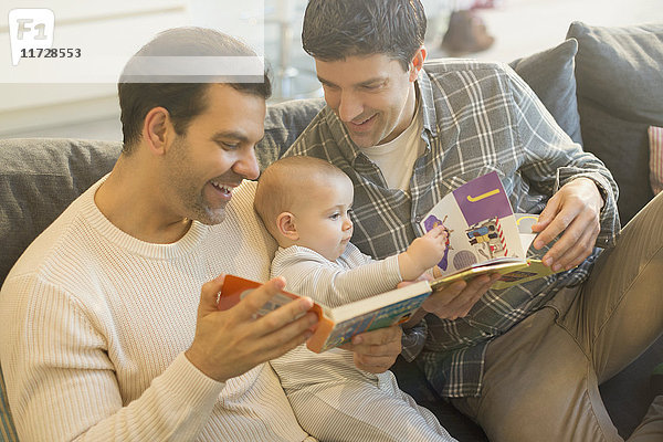Männliche schwule Eltern lesen Buch zu Baby-Sohn auf Sofa