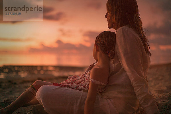 Gelassene Mutter und Tochter entspannen am Strand in der Abenddämmerung