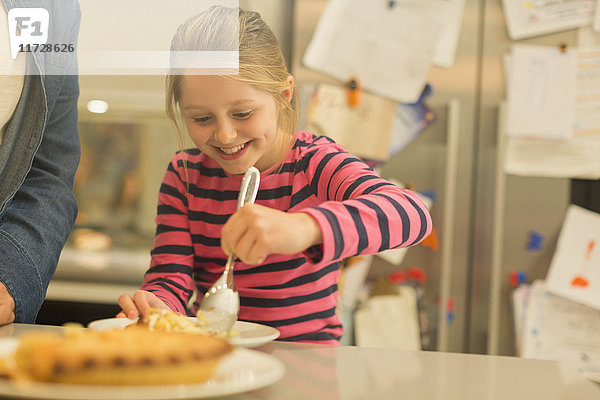 Lächelndes  eifriges Mädchen  das Kuchen in der Küche serviert.