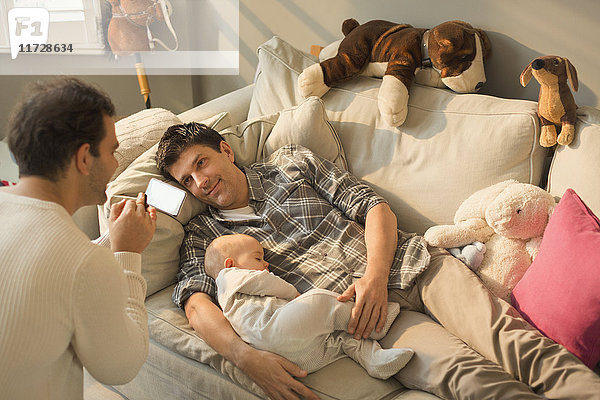 Männliche schwule Eltern und Baby-Sohn auf dem Wohnzimmer-Sofa