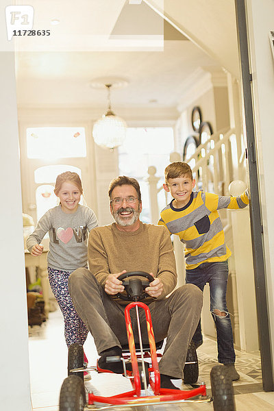 Portrait lächelnde Kinder schieben Vater auf Spielzeugauto im Foyer Flur