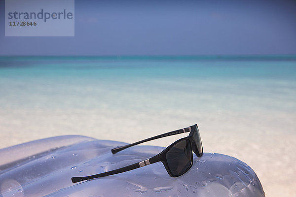 Sonnenbrille auf aufblasbarem Floß im tropischen blauen Ozean