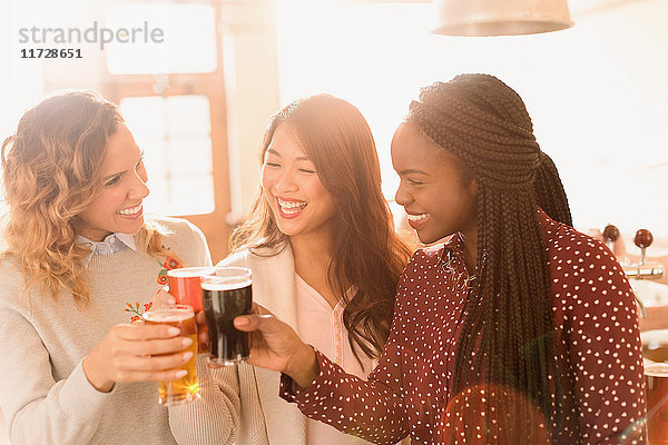 Freundinnen stoßen mit Biergläsern in einer Bar an