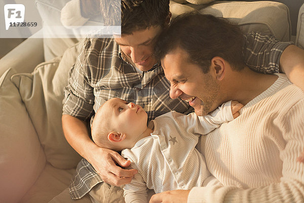 Blick von oben männliche schwule Eltern kuscheln mit süßem Baby-Sohn auf Sofa