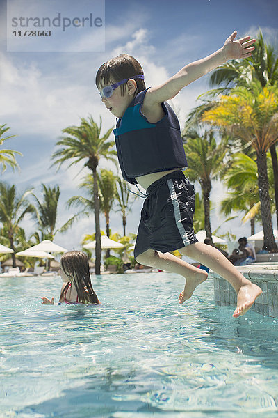 Junge springt in sonniges tropisches Schwimmbad