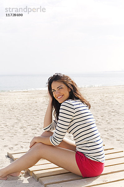 Porträt einer schönen brünetten Frau  die am Strand sitzt