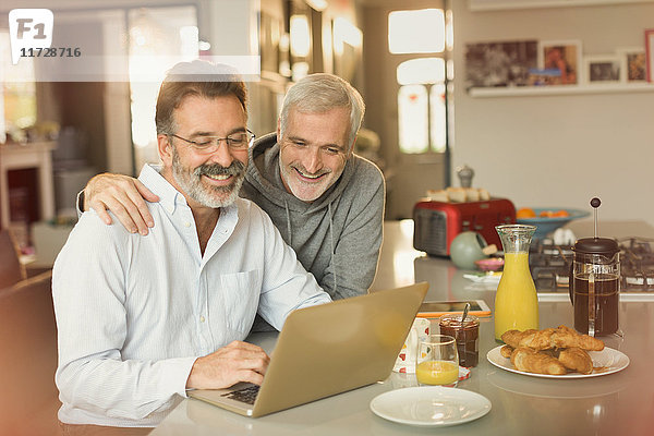 Männliches schwules Paar mit Laptop und Frühstück am Küchentisch