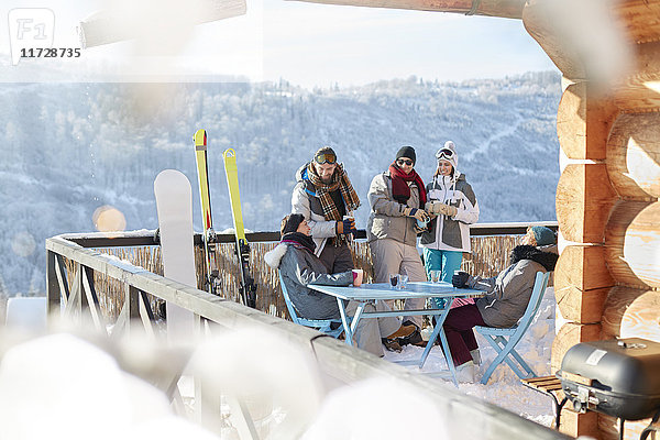 Skifahrer- und Snowboarderpaare hängen auf dem sonnigen Hüttenbalkon Apres-Ski.