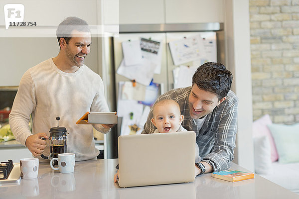 Männliche schwule Eltern und Baby-Sohn mit Laptop und Digital-Tablett in der Küche