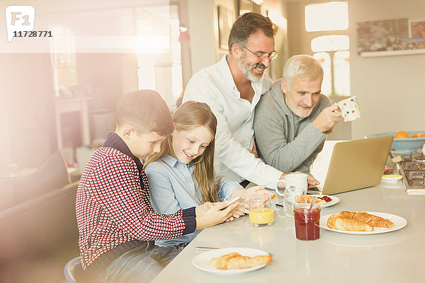 Schwule Eltern und Kinder mit Laptop und Handy  Frühstücken in der Küche
