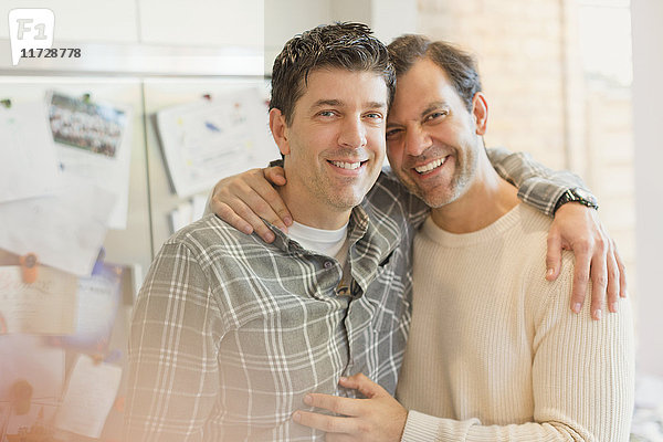 Porträt lächelndes  liebevolles männliches schwules Paar  das sich in der Küche umarmt.