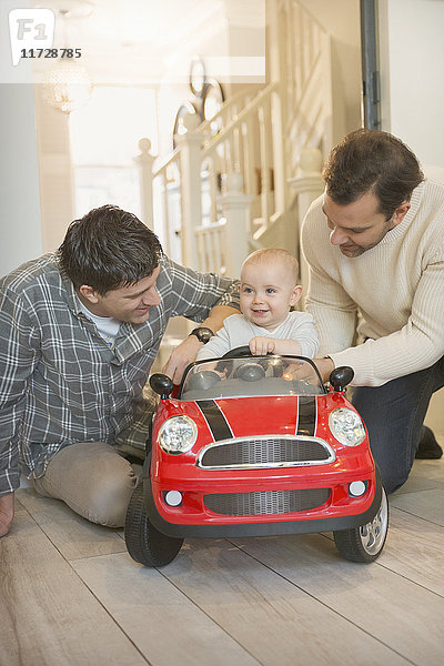 Männliche schwule Eltern und Baby-Sohn spielen mit Spielzeugauto