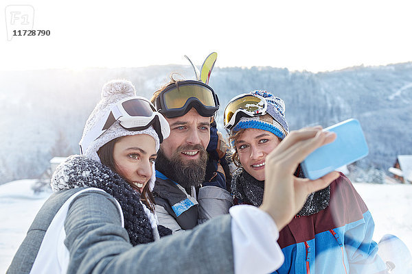 Skifahrerfreunde nehmen Selfie mit Fotohandy im Schneefeld mit