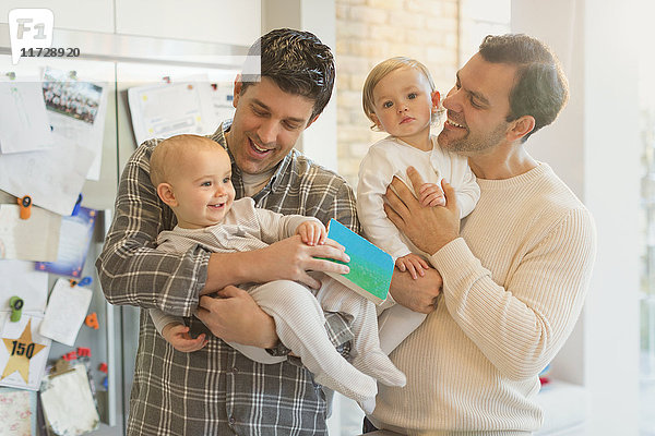 Männliche schwule Eltern halten Babysöhne in der Küche.