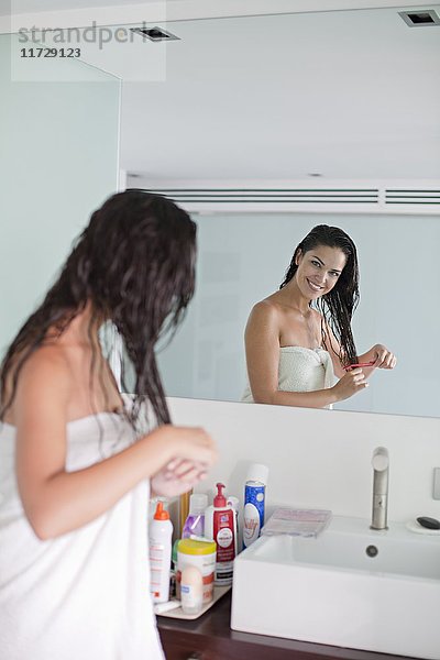 Brünette Frau bürstet ihr Haar vor dem Spiegel
