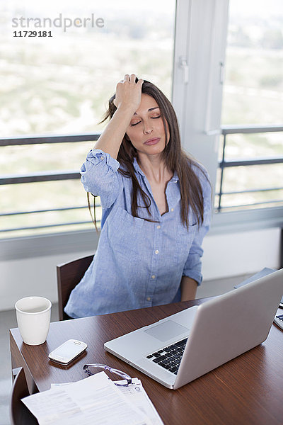 Frau mit Kopfschmerzen vor dem Computer