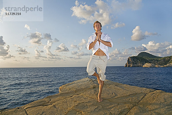 Mann beim Yoga in einer Klippe am Meer