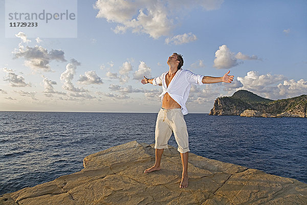 Ein Mann  der seine Arme in einer Klippe auf Ibiza ausstreckt.