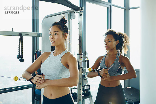 Zwei junge Frauen trainieren im Fitnessstudio und benutzen dabei Fitnessgeräte