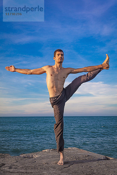 Junger Mann im Freien  in Yogastellung  auf einem Bein balancierend