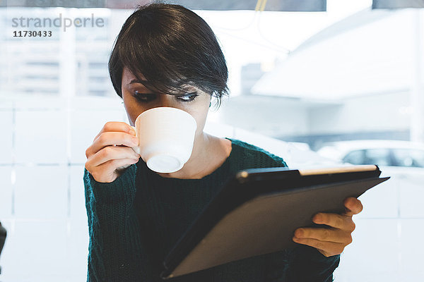 Frau im Café  die sich ein digitales Tablet anschaut und Kaffee trinkt