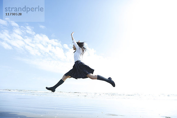 Junge Japanerin in Highschool-Uniform springt am Meer  Chiba  Japan
