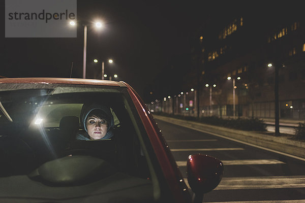 Frau  die nachts am Straßenrand der Stadt aus der Windschutzscheibe eines Autos schaut