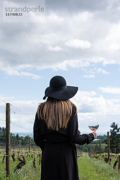 Frau steht im Weinberg  hält ein Glas Wein  Rückansicht