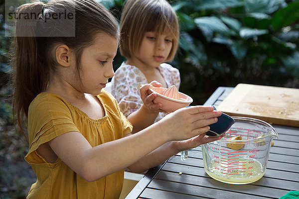 Zwei junge Schwestern gießen Zitronensaft für Limonade am Gartentisch