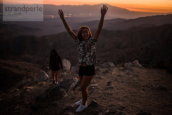 Porträt einer jungen Frau mit erhobenen Händen im Joshua-Tree-Nationalpark bei Sonnenuntergang  Kalifornien  USA