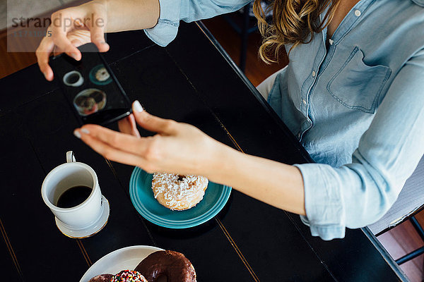 Draufsicht einer Frau  die ein Doughnut-Loch und Kaffee auf dem Tisch fotografiert