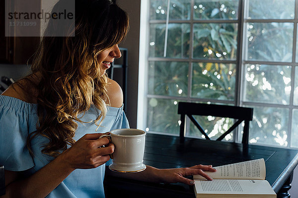 Junge Frau liest Buch bei Tisch