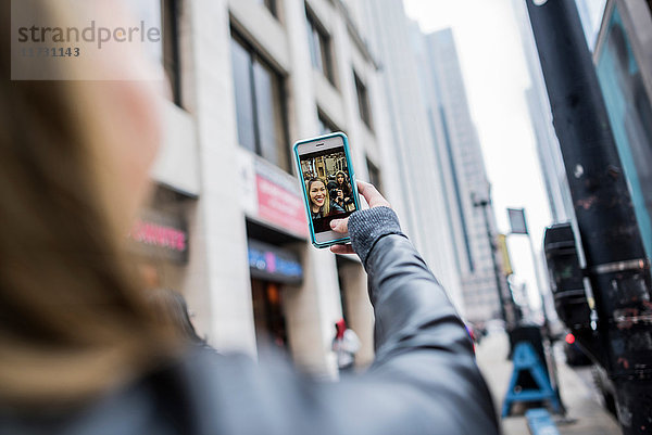 Junge Frau  im Freien  mit Smartphone in der Hand  bei Videoanruf  Rückansicht