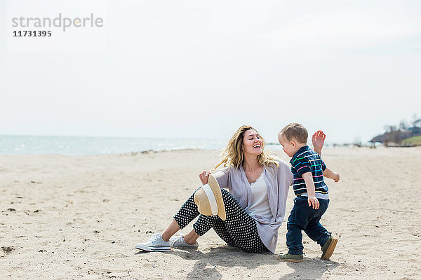 Junge Frau sitzt am Strand und spielt mit Kleinkind