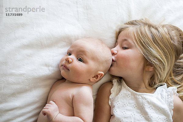 Draufsicht auf junges Mädchen und kleinen Bruder  die auf dem Bett liegen  Mädchen küsst kleinen Bruder