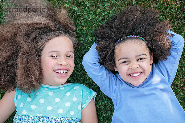 Porträt von zwei jungen Mädchen  im Gras liegend  lachend  Draufsicht