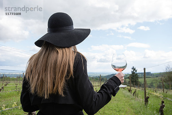 Frau steht im Weinberg  hält ein Glas Wein  Rückansicht