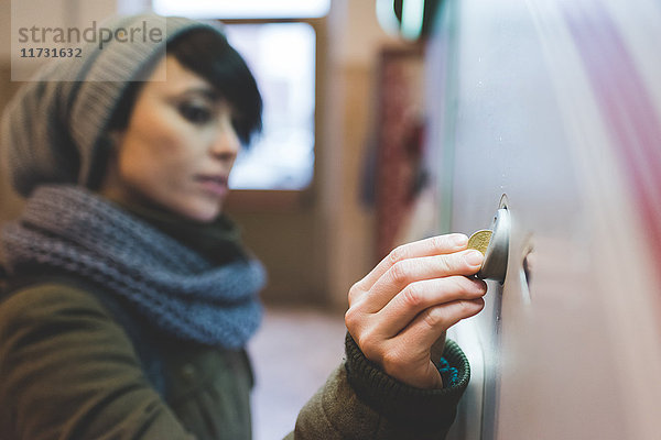 Frau mit Strickmütze wirft Münze in den Fahrkartenautomaten
