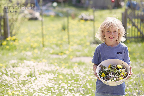Porträt eines Jungen  der eine Schale mit Gartenkräutern hält