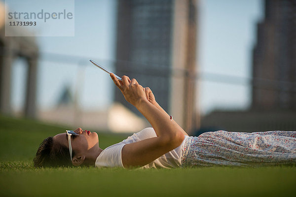 Mittelgroße erwachsene Frauen liegen im Park und verwenden ein digitales Tablett