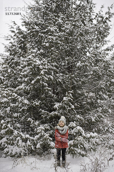 Junges Mädchen steht vor einem großen immergrünen  schneebedeckten Baum