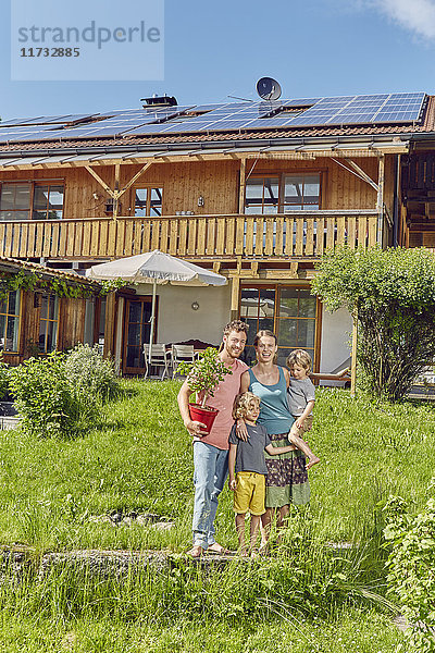 Porträt einer jungen Familie  die eine Topfpflanze hält und vor einem Haus mit Solarzellendach steht