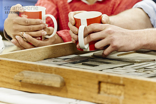 Nahaufnahme von männlichen und weiblichen Händen beim Kaffeetrinken in der traditionellen Druckwerkstatt