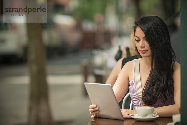 Mittelgroße erwachsene Frauen mit digitalem Tablet im Straßencafé