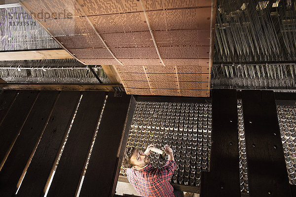 Draufsicht eines männlichen Webers mit alter Webmaschine in einer Textilfabrik